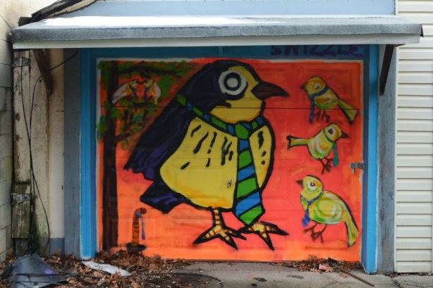 birds painted on a garage door, stylized, large bird wearing a long necktie and smaller birds with similar ties, all on an orange background