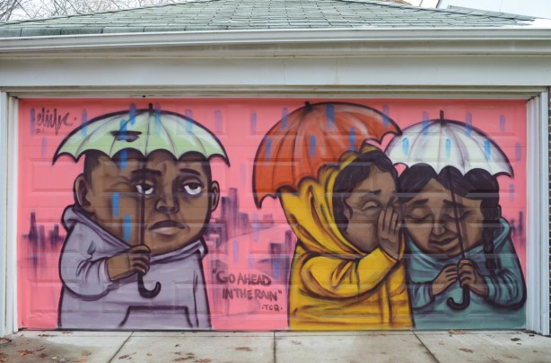 mural by elicser elliott on a garage door in an alley, people under umbrellas in the rain, pink background