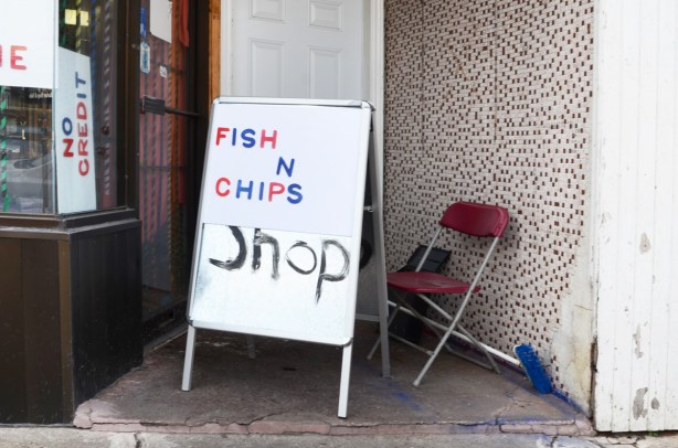 fish and chips shop sign on a store doorstep along with a folding chair
