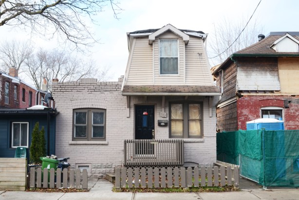 small house with brown picket fence in front, second story with mansard roof on one part of house only 