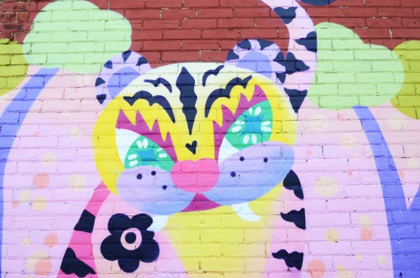 a June Kim mural of a tiger or cat, feline, on a brick wall in an alley