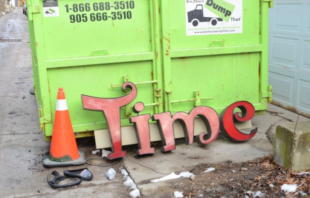 leaning against a lime green dumpster is the time part of an old coffee time donut shop sign