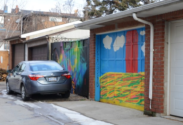 car parked in front of two murals on garage doors, breaking bread is one of the murals