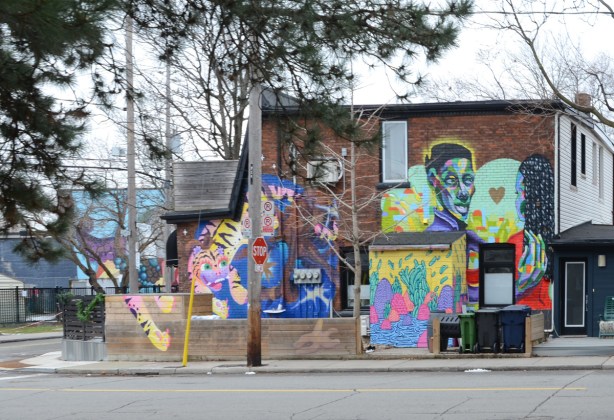 the side of a house is covered with street art, 2 or 3 murals on both upper and lower storeys