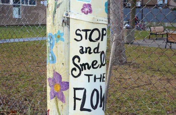 wood utility pole painted white and decorated with flowers and a sign that says stop and smell the flowers
