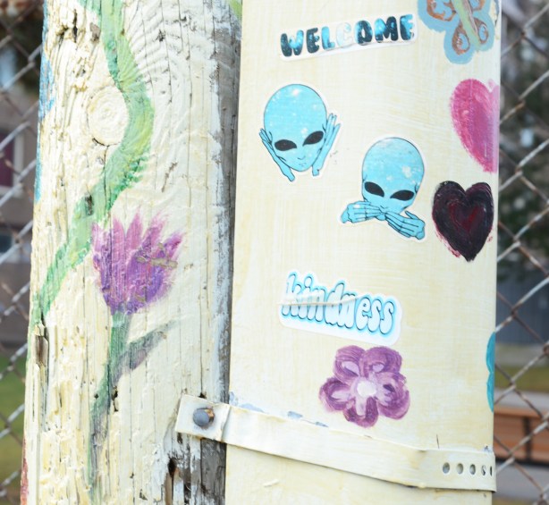 white pole with purple flower painted on it, also some stickers, welcome, kindness