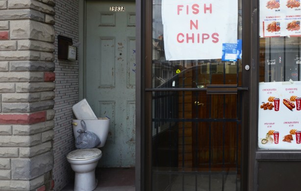 old toilet on the doorstep of an apartment beside a fish and chips store