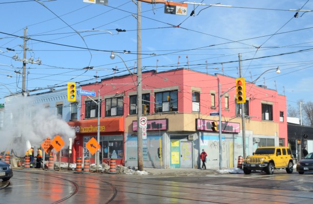 pink two storey building on the northeast corner of Coxwell and Eastwood, with construction in front, Coffee Time on the lower level is closed and windows papered over