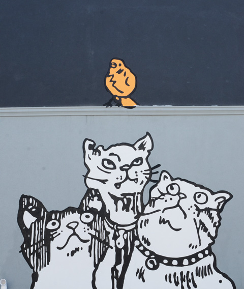large mural in a Little India alley, three white cats looking up at a yellow bird on a ledge