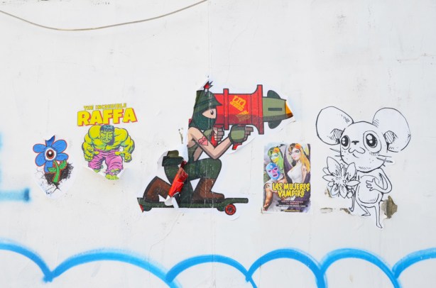 stickers and pasteups on a white wall. Urban ninja squadron t bonez on one knee with a large missle launcher on one shoulder