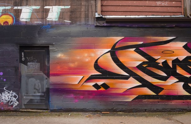 in an alley, a door painted black, part of a callligraphy mural with black writing on magenta and orange background