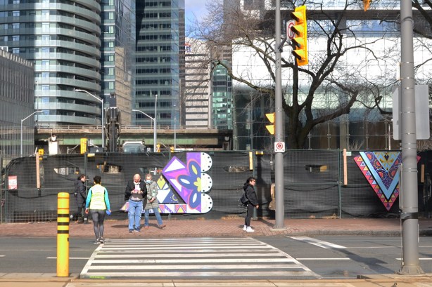 waiting to cross Queens Quay at York, by black hoardings around redevelopment of Love Park, 