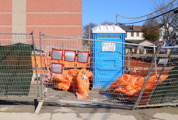 construction fence leaning outward, posters, porta potty, construction site