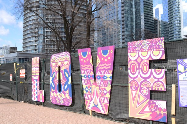 large letters, L O V E spell love on black haordings, letters are decorated in abstract patterns in pink, yellow, and blue