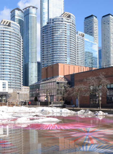 ice melting on skating rink by power plant, pink and blue designs painted on the concrete below, highrises in the background, looking northeast from walkway by waterfront