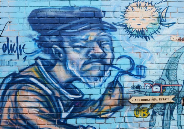 in blues, mural by elicser of an older man with white beard, a hook for a hand, smoking a pipe, wearing a cap