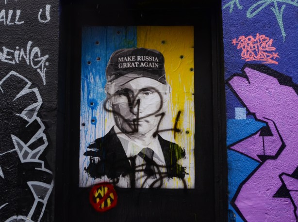 street art portrait of Putin in grey tones, wearing a baseball cap that says Make Russia Great Again, background is half blue and half yellow for Ukraine. It has already been scribbled on 