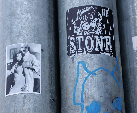 small black and white sticker graffiti on pole, picture of man in a mask holding shoulders of a woman