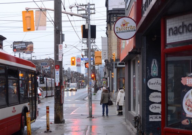 an older couple walking on sidewalk on Queen West waiting for greenlight at Bathurst by taccorito restaurant