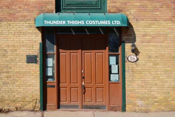entrance to thunder thighs costume ltd, with green awning over brown double doors. 