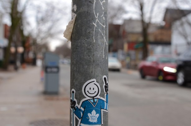 sticker on a pole, a stick figure person with a happy face and a realistic blue Maple leafs hockey jersey