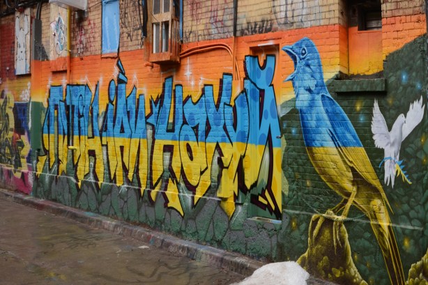 mural in Rush Lane in blue and yellow, text in Cyrillic alphabet, bird, white dove with branch that is half yellow and half blue