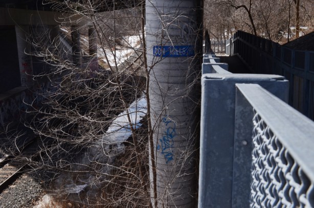 blue sign on a concrete pillar that says Don Mills Road, beside a metal ramp walkway under a bridge, Lower Don Trail