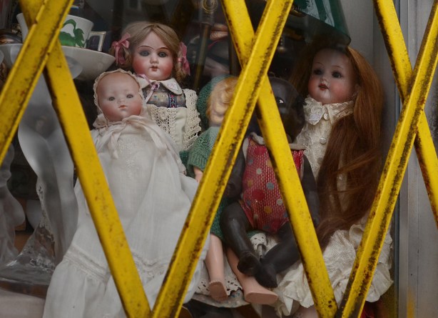 a collection of dolls in a store window with yellow metal grille in front