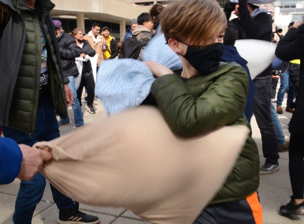people participating in pillow at nathan phillips square, outdoors, fighting with pillows, boy in green jacket and black covid mask