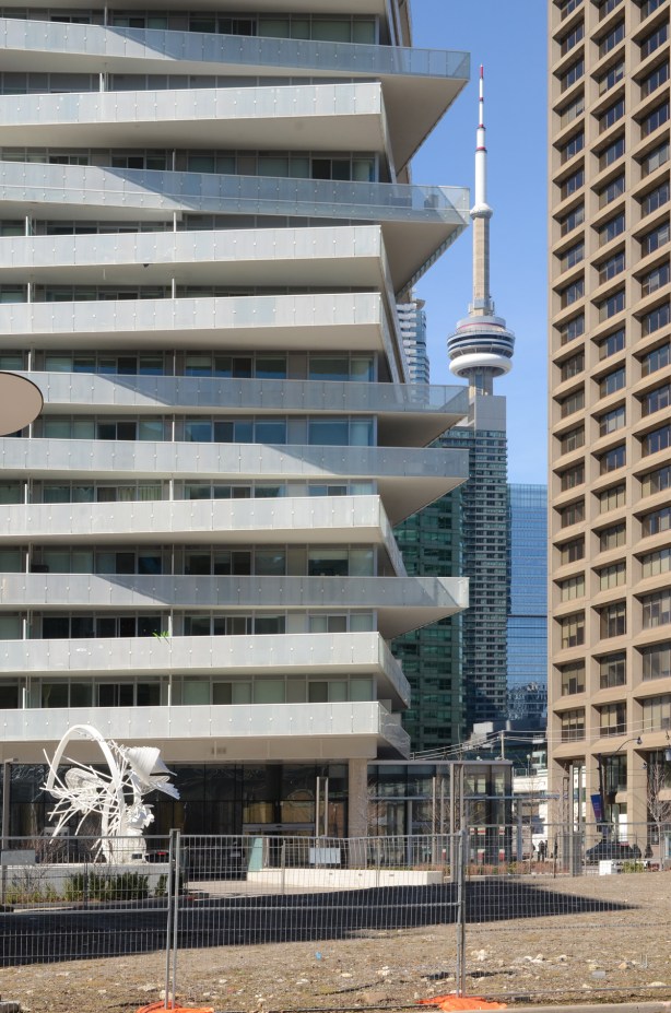 CN Tower in the background, peaking through between a new glass and metal condo with different angled balconies, and an older concrete highrise 
