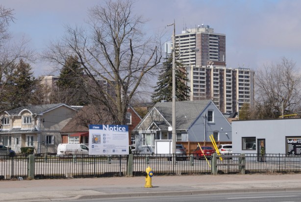 blue and white development notice sign on vacant lot on yonge street, houses, and newer highrises in the background, residential area, Newtonbrook
