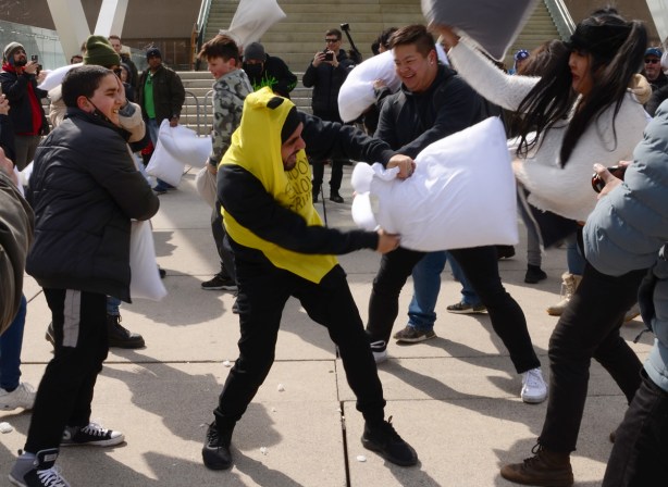 people participating in pillow at nathan phillips square, outdoors, fighting with pillows, man with yellow over his head like a banana