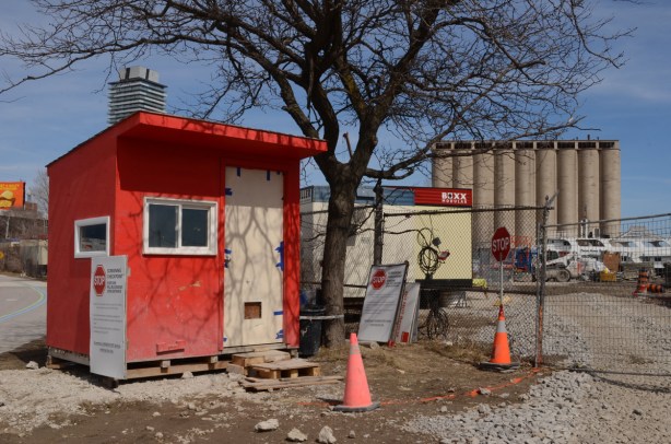 small red cabin beside entrance to parking lot and construction site, concrete silos in the background