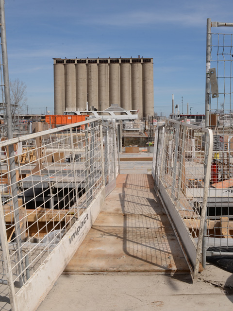 small temporary bridge, concrete silos in background, construction fence in front, 