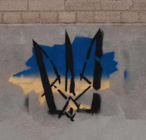 spray paint stencil graffiti, black trident on blue and yellow map of ukraine