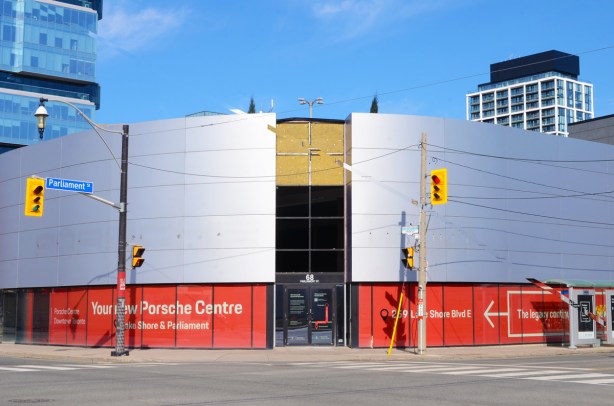 Now empty, the porsche dealership at Parliament and Front, large shiny silver curved surface on upper levels, window with red coverings on the ground floor. 