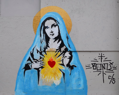 a painting of the madonna, Mary, in blue robes, with gold halo, and red heart in chest gold light rays coming from red heart, painting on a wall