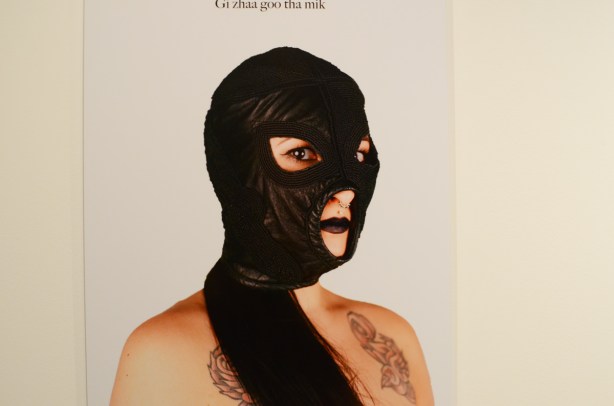 photo of upper torso and head of a woman with tattoos, blackish lipstick and heavy eye makeup, wearing a black bdsm type mask covering most of her head and face. beaded black leather fetish mask 