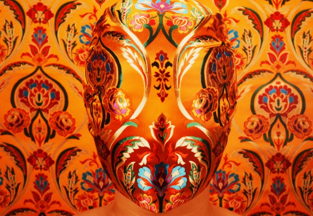 elaborately embroidered mask, reds and greens and black on orange background