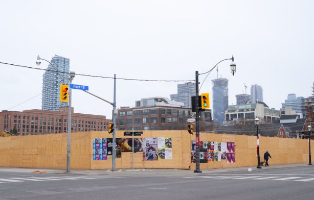 plywood hoardings covering the southwest corner of Front Street and Parliament Street, some posters on the plywood, skyline in the background
