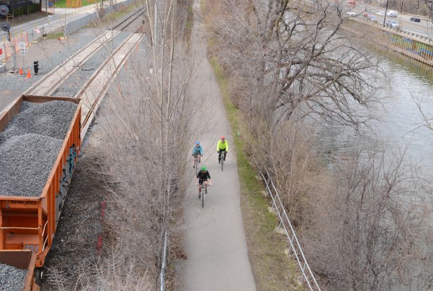 looking north from bridge on Queen East over the Don River, train car on tracks, cyclists on bike path, river, and traffic on DVP
