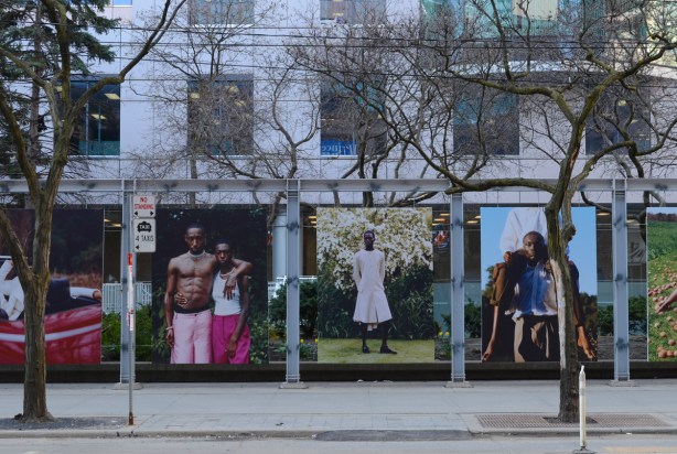 3 of the portraits in Cultural Turns exhibit outside Metro Hall, on the left a couple - man in pink shorts has his arm around the womans shoulders