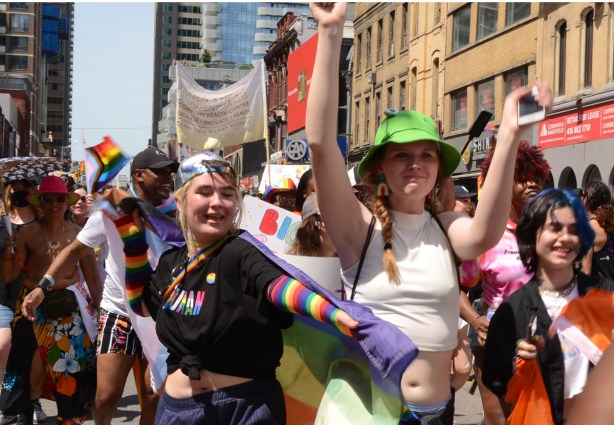 dyke march 2022 people marching, one in a green hat, one with rainbow sleeves