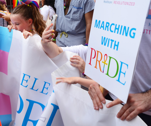 young girl helping to hold white banner, marching with pride, other hands holding the banner too, toronto pride parade 2022