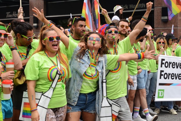 group cheering and blowing whistles, arms up, getting ready for pride parade, TD canada trust group in green t shirts with rainbows on them