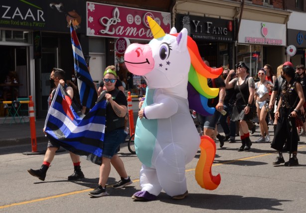 dyke march, people with trans flag walking beside someone in an inflatable unicorn costume