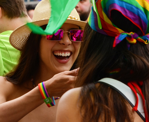 woman in magenta glasses and cowboy hat laughing with woman with rainbow bandana over her head