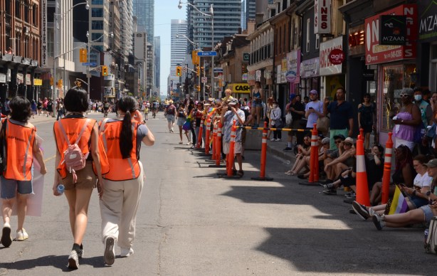 three women in orange vests walking parade route with crowds on the sidewalk