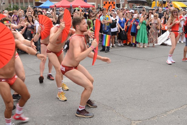 some members of triggerfish in their speedo suits, dancing with red fans 