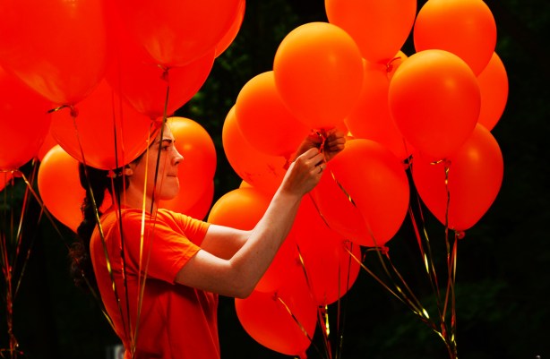 young woman tying orange balloons to a pride parade float, NDP float, she's wearing orange too